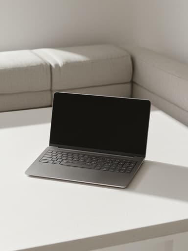 미니멀한 흰색 라운지 테이블 위에 세련된 노트북, 부드러운 자연광이 미세한 그림자를 드리우며, 매끄러운 금속 표면에 약간의 반사가 있는 모습, 현대적인 패브릭이 배경에 있는, 고요하고 현대적인 분위기.