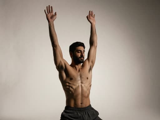 30대 중동계 남성이 편안한 요가복을 입고, 평온한 표정을 지으며 팔을 위로 뻗고 있는 요가 자세를 취하고 있는 모습의 반신 사진. 부드러운 조명이 있는 현대적인 사진 스튜디오 배경.