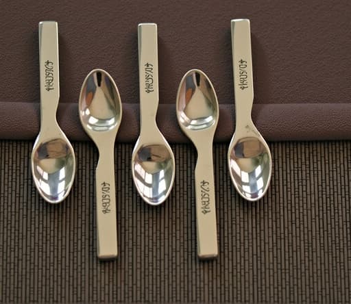 부드러운 질감의 매트 위에 우아한 스테인리스 스틸 수저 세 개가 아름답게 배열되어 있으며, 부드러운 자연광이 비추어 따뜻하고 아늑한 분위기를 연출합니다.