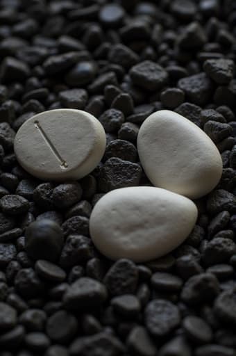 이미지에는 두 개의 매끄러운 흰색 알약이 불규칙한 검은색 돌무더기 위에 놓여 있습니다. 돌의 자연적인 질감이 알약의 순수함을 강조하며, 차분하고 사색적인 분위기를 자아냅니다.