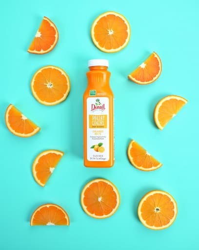 밝고 통풍이 잘 되는 주방의 나무 테이블 위에 신선하게 짜낸 오렌지 주스가 담긴 유리컵이 놓여 있습니다. 주스는 생생한 주황색이며, 유리잔 주위에 여러 개의 오렌지 슬라이스가 예쁘게 배열되어 있어 신선함을 더하고 있습니다. 창문을 통해 햇살이 비치며 따뜻하고 초대하는 분위기를 만들어냅니다.