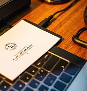 세련된 나무 책상 위에 놓인 흰색 명함의 클로즈업 뷰로, 배경에는 흐릿하게 보이는 스타일리시한 노트북과 사무용 아이템들이 있다. 명함은 우아한 타이포그래피와 미니멀한 디자인으로 로고와 연락처 정보를 보여준다. 전체적인 분위기는 전문적이고 세련된 느낌을 전달한다.