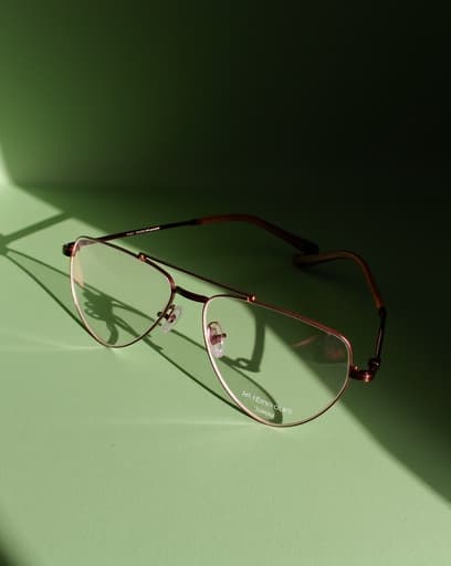 세련된 디자인의 안경 한 쌍이 부드러운 녹색 표면 위에 우아하게 놓여 있으며, 가벼운 프레임과 자외선 차단 렌즈가 강조되고 있습니다. 녹색 배경은 신선하고 자연스러운 느낌을 더하며, 안경의 현대적인 미학을 향상시킵니다.