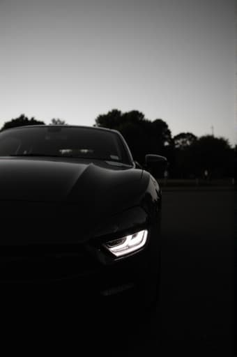 조용한 교외 도로의 한쪽에 주차된 세련된 현대적인 자동차. 맑은 파란 하늘 아래 울창한 녹색 나무로 둘러싸여 있습니다. 햇빛이 자동차의 광택있는 표면에 반사되어 스타일리시한 특징을 강조합니다.