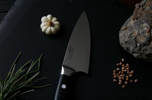 매끄러운 검은 표면 위에 놓인 고급 주방용 칼. 칼날은 빛나는 스테인리스 스틸로 제작되었으며, 인체공학적인 손잡이가 편안함과 디자인을 잘 보여준다. 배경은 어두워서 칼에 모든 시선을 집중시키며, 요리의 우아함과 정밀함을 느끼게 한다.