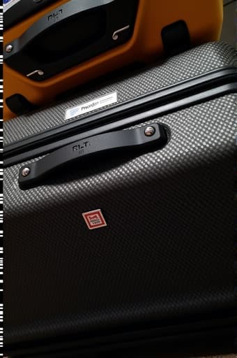 공항 터미널에 세워진 멋진 노란색과 검은색의 여행가방이 강조되어 있으며, 내구성 있는 하드쉘과 네 개의 스피너 바퀴가 잘 보입니다. 밝은 색상은 세련되고 현대적인 환경과 대조를 이루며, 여행객들과 체크인 카운터가 있는 배경이 그려집니다. 이 이미지는 모험과 여행에 대한 준비가 느껴집니다.