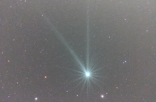 어두운 별이 빛나는 하늘을 가로지르는 혜성의 생생한 이미지로, 빛나는 입자와 가스로 이루어진 화려한 꼬리를 보여주며, 먼 별들과 희미한 성운으로 둘러싸여 경이롭고 신비로운 분위기를 자아냅니다.