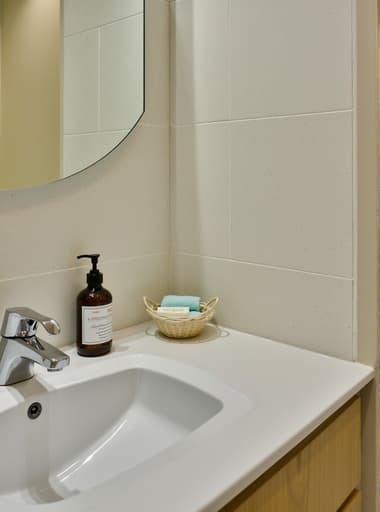 세련되고 현대적인 욕실 세면대가 스타일리시한 거울과 장식적인 비누 디스펜서를 특징으로 하고 있습니다. 세면대는 고품질 세라믹으로 만들어졌으며, 거울은 조정 가능하여 밝고 통풍이 잘 되는 욕실 환경이 반사되고 있습니다. 부드러운 자연광과 밝은 색상의 타일로 장식되어 있습니다.