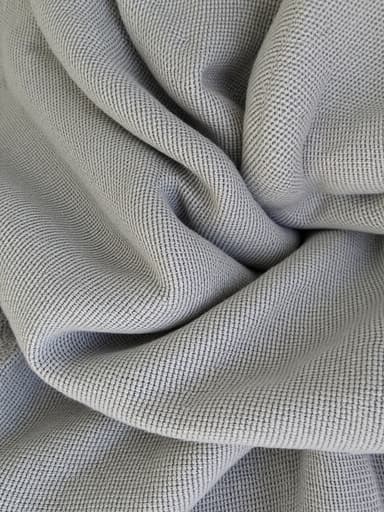 부드러운 질감과 복잡한 직조를 보여주는 회색 직물의 클로즈업 샷입니다. 이 직물은 중립적인 색상의 배경에 부드럽게 확산된 조명을 받아 세련되고 차분한 분위기를 만들어냅니다.