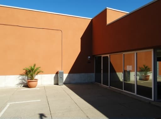 밝고 현대적인 오렌지색 건물이 맑은 파란 하늘을 배경으로 두드러지게 서 있으며, 생생한 색상과 세련된 건축 디자인을 자랑합니다. 주변 환경은 푸른 식물과 다른 건물들로 가득 차 있어 도시의 분위기를 더욱 돋보이게 합니다.