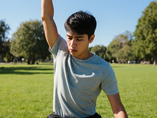 10대 초반의 라틴계 남성이 편안한 티셔츠와 운동복 바지를 입고 반신 촬영을 하고 있습니다. 그는 한쪽 팔을 위로 올리고 다른 팔은 옆으로 뻗으며, 약간 슬픈 표정을 지은 채 스트레칭을 하고 있습니다. 배경은 푸른 하늘과 푸른 잔디가 있는 평화로운 야외 공원입니다.