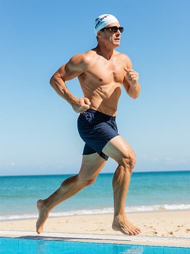 40대 유럽계 남성이 햇살이 내리쬐는 수영장 가장자리를 따라 달리며 수영복, 수영 모자, 선글라스를 착용하고 자신감과 열정을 발산하고 있습니다. 배경에는 청명한 바다와 밝은 하늘이 어우러진 멋진 해변 풍경이 펼쳐져 있습니다.
