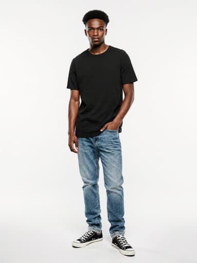 세련된 티셔츠와 청바지를 입고 한 손은 주머니에 넣은 채 자신감 있게 서 있는 10대 초반의 아프리카계 남성의 전신 사진. 깔끔한 화이트 스튜디오 배경에서 현대적이고 패셔너블한 느낌을 발산하고 있습니다.