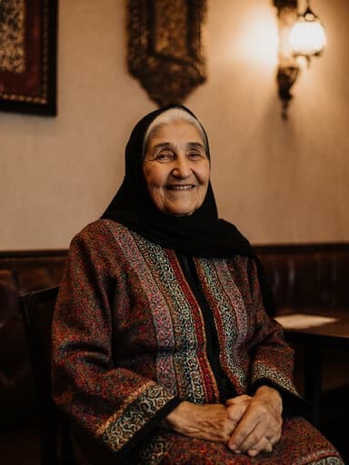 평온한 표정을 짓고 있는 중동계의 노인이 전통 의상을 입고 아늑한 카페에 앉아 무릎에 손을 올리고 행복한 감정을 표현하며 따뜻하고 초대하는 분위기를 자아내고 있습니다.