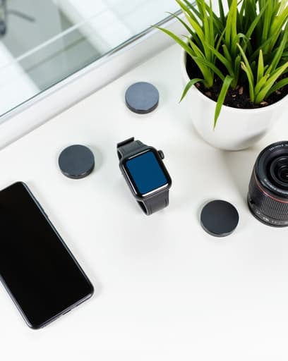 세련된 스마트폰, 고해상도 디지털 카메라, 그리고 생기 넘치는 초록색 화분이 있는 밝고 현대적인 실내 작업 공간. 물건들이 미니멀한 책상 위에 정돈되어 있으며, 자연광이 장면을 비추어 신선하고 창의적인 분위기를 자아냅니다.