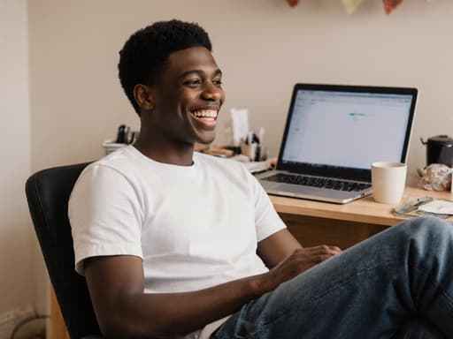 10대 초반의 흑인 남성이 편안한 티셔츠와 청바지를 입고 아늑한 집 사무실에 앉아 있습니다. 그는 고객과의 소통을 암시하며 밝은 미소를 지으며 노트북을 바라보고 있습니다. 배경에는 노트북과 커피 컵이 놓인 깔끔한 책상이 있어 따뜻하고 초대하는 분위기를 더합니다.